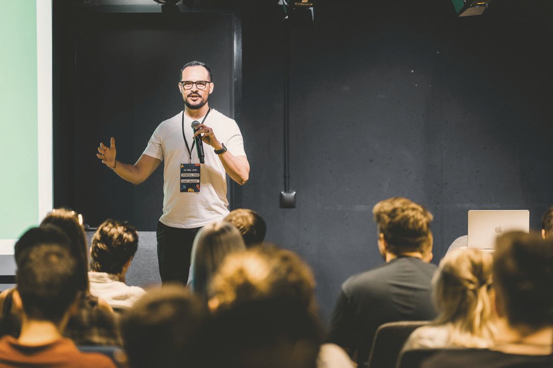 Francesco Prano on stage at a Clay Club event, speaking into a hand microphone, with an audience seated in front of him.